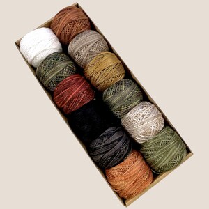 May include: A box of 12 spools of embroidery floss in various colors, including white, brown, green, black, and orange. The spools are arranged in a row in the box.