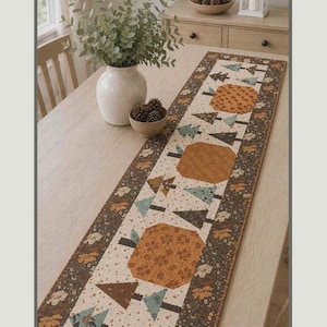 May include: A rectangular table runner titled Chasing Autumn Runner measuring 12 inches by 46 1/2 inches. The fabric features a central cream panel with orange pumpkin shapes and teal and brown tree motifs, bordered by a dark brown floral print fabric.