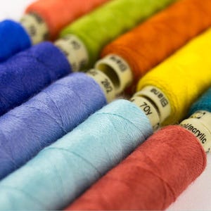 May include: A collection of colorful spools of thread, including blue, purple, light blue, turquoise, orange, yellow, and red. The spools are labeled with the length of the thread in yards.