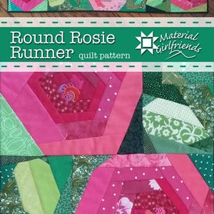 May include: A quilted table runner featuring a floral design with pink and red roses. The runner has a green border and includes the text "Round Rosie Runner quilt pattern" and the "Material Girlfriends" logo.