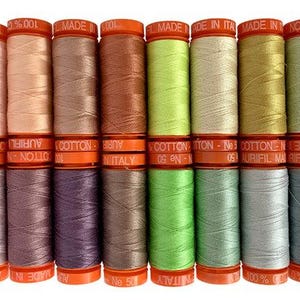 May include: A collection of 18 spools of cotton thread in various shades of pink, orange, brown, green, and blue. The spools are labeled "Aurifil" and "Made in Italy".