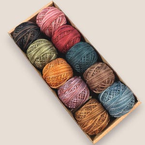 May include: A set of ten balls of embroidery floss in a variety of colors, including pink, red, green, blue, and brown. The balls are arranged in a box.