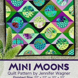 May include: A colorful quilt with a geometric design featuring circles and diamonds in shades of green, blue, purple, and yellow. The quilt measures 22 inches by 22 inches or 20 inches by 20 inches. The text "MINI MOONS" is displayed at the bottom.