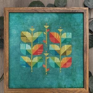 May include: A square wooden frame containing a cross stitch design titled Madras Beanstalk by Robin Pickens. The embroidery features two vertical stems with stylized, multi-colored geometric leaves in shades of red, yellow, blue, and green on a mottled teal fabric background.