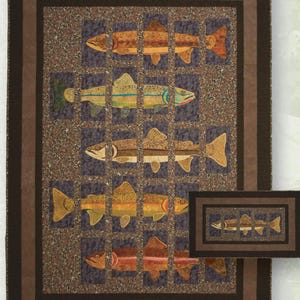 May include: A quilted wall hanging featuring a grid of colorful fish. The fish are in shades of brown, orange, yellow, and green, set against a dark blue-gray background. The quilt has a brown border and a smaller, framed version is also visible.