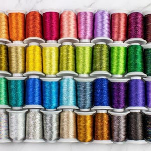 May include: A collection of 40 spools of metallic thread in various colors, including gold, silver, red, blue, green, and purple. The spools are arranged in four rows of ten, and each spool has a white plastic bobbin.