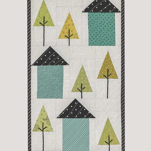 May include: A fabric quilt titled "Tiny Town" featuring stylized houses and trees. The houses have teal walls and black polka-dot roofs. The trees are yellow and green. The quilt measures 11 inches by 18.5 inches.