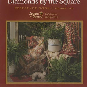 May include: A book cover titled "Diamonds by the Square" with the subtitle "Reference Book | Volume Two." The cover features a quilt display with ferns and a rabbit statue. The text "Square in a Square" and "Technique by Jodi Barrows" are also visible.