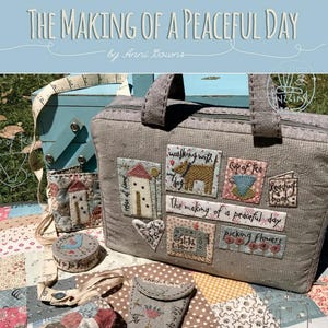 May include: A gray fabric bag with a zipper and handles, decorated with embroidered patches depicting scenes of a peaceful day, such as a cup of tea, reading a book, and walking a dog. The bag is surrounded by other fabric crafts, including a small round pincushion and a needle case. The text "The Making of a Peaceful Day" is printed on the bag.