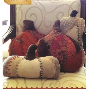 May include: A trio of handcrafted fabric pumpkins in various sizes and colors, including orange, red, and cream. Each pumpkin features a dark brown stem and unique patchwork or stitched details. The text "Crazy Pumpkin Trio" is visible.