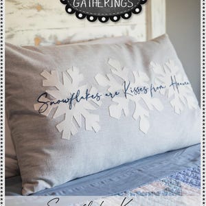 May include: A rectangular gray pillow with white snowflake appliqués and the text "Snowflakes are Kisses from Heaven" in navy blue. The pillow measures 18 x 30 inches.