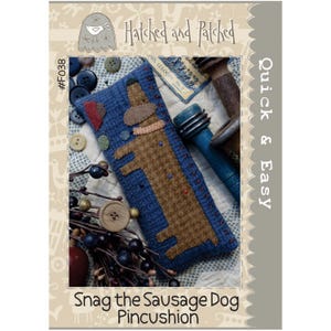 May include: A blue pincushion with a brown dachshund design. The pincushion is rectangular and features the text "Snag the Sausage Dog Pincushion." The image also includes the text "Hatched and Patched" and "Quick & Easy."