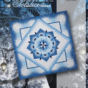 May include: A quilt with a geometric starburst design in shades of blue and white. The quilt is labeled "Summer Solstice Queen" and is part of the "Traditions Collection" by Timeless Treasures. The quilt is made using foundation paper piecing.