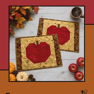 May include: Two rectangular quilted placemats featuring a central red apple motif on a gold background with a dark patterned border. The text Apples Mellow, Tamara Cook for Villa Rosa Designs is visible on the red and orange background.