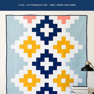 May include: A geometric quilt with a navy blue border and a pattern of white, yellow, and navy blue crosses. The quilt has a light blue background and pink accents. The text "ANDES ODE" and "COTTON + JOY" are at the top.