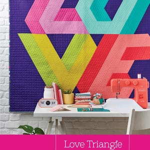 May include: A quilted wall hanging with the word "LOVE" in geometric shapes, featuring pink, teal, yellow, and red colors. A sewing machine and craft supplies are on a white table. The text "Love Triangle" is displayed.