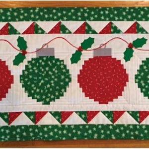 May include: A rectangular Christmas table runner featuring four large, stitched ornaments in red and green. The ornaments are connected by a red string with holly accents. The border is green with white stars and red and white triangles.