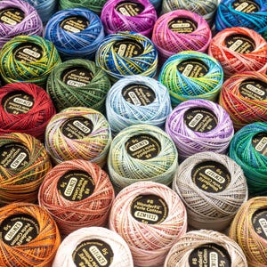 May include: A collection of small, round balls of WonderFil Perle Cotton thread in various colors. Each ball features a black label with white text indicating the thread is 100% Egyptian cotton, size 8, and weighs 5 grams per unit.
