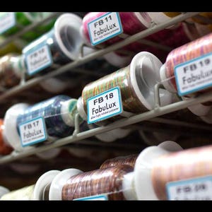 May include: Close-up of spools of colorful thread with labels that read "Fabulux" and "FB 11", "FB 18", "FB 19", and "FB 17".