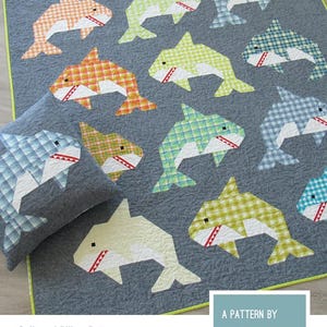 May include: A gray quilt and pillow set featuring patchwork sharks in various colors and patterns. The text "SOCIAL SHARKS" is at the top. The pattern is by Elizabeth Hartman. The quilt and pillow pattern includes instructions for making a quilted pillow cover and two quilt sizes.