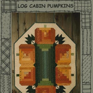 May include: A quilted wall hanging featuring log cabin pumpkins. The pumpkins are made of orange, yellow, and brown fabric, with green stems and leaves. The background is a light beige, and the text "SUZANNE'S ART HOUSE LOG CABIN PUMPKINS" is at the top.