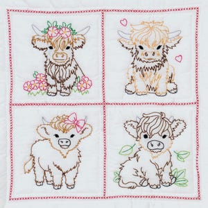 May include: A white quilted fabric square divided into four sections by red cross-stitch borders. Each section features a machine-embroidered Highland cow in brown and black thread, accented with pink flowers, a pink bow, or green leaves.