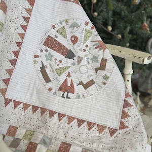 May include: A white and red patchwork quilt with a circular design in the center. The design features a Santa Claus figure, a reindeer, and the words "Merry Christmas" and "Peace". The quilt is trimmed with a red and white scalloped border.