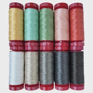 May include: A collection of twelve spools of Aurifil cotton thread in various colors. The spools are arranged in three rows of four, with colors including yellow, teal, green, pink, and red. The spools have red caps and are labeled "100% Cotton" and "Made in Italy."