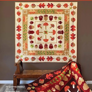 May include: A cream-colored quilt with a square design, featuring autumn leaves, acorns, and mushrooms in shades of red, orange, and brown. The quilt is 72.5 x 72.5 inches and is labeled "Oak Grove Square" and "Medallion Quilt."