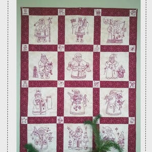 May include: A Christmas-themed quilt featuring embroidered Santa Claus figures in various poses. The quilt has a burgundy border and a grid pattern with Santa Claus designs. The text "Bird Brain Designs" is at the top, and "Here Comes Santa Quilt" is at the bottom.