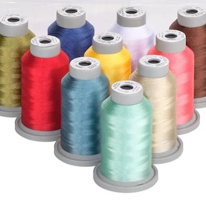 May include: Assortment of ten spools of embroidery thread in various colors, including green, red, blue, yellow, white, brown, and beige. The spools are arranged in a semi-circle on a white surface.