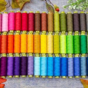 May include: A collection of colorful spools of thread, arranged in a rainbow pattern. The spools are all the same size and shape, and they are made of a variety of materials, including cotton and polyester.