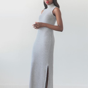 May include: A sleeveless, light gray maxi dress with a high neckline and a side slit. The dress is paired with black ankle boots and a black headband. The text "NIKKO TOP & DRESS" is at the top, with "sewing pattern | sizes 0 - 18" below.