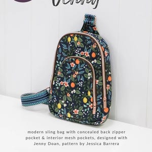 May include: A navy blue sling bag with a floral pattern of oranges, lemons, and flowers. The bag has a concealed back zipper pocket and interior mesh pockets. The bag is designed by Jenny Doan and is a modern style.