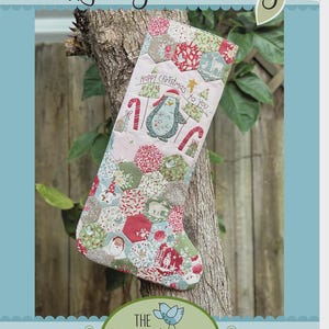 May include: A quilted Christmas stocking with a penguin design. The stocking features a patchwork pattern with red, green, and white fabrics. Text on the stocking reads "Happy Christmas to You" and "Happy Penguin Stocking". The Birdhouse Patchwork Designs logo is at the bottom.
