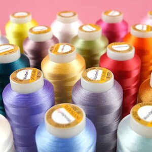 May include: A close-up of a variety of spools of thread in different colors, including purple, blue, yellow, red, and green. The spools are labeled with the brand name "WonderFil" and the text "Invisafill".