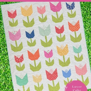 May include: A quilt pattern featuring a tulip design. The quilt showcases colorful tulips in shades of pink, orange, yellow, blue, and red, with green stems and leaves, set against a white background. The finished quilt size is 56" x 70".