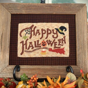 May include: A framed embroidery with a rustic wooden frame. The embroidery is on a brown fabric and features the text "Happy Halloween" in a whimsical font. The embroidery also includes a witch's hat, a pumpkin, candy corn, and a broom.