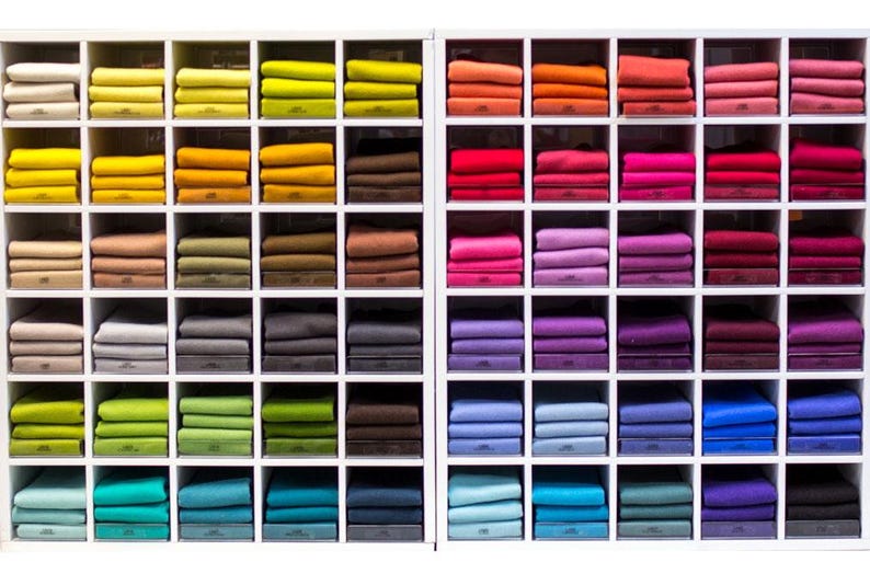 Puede incluir: Una estanter&iacute;a blanca con 10 filas de cuadrados de tela de colores. Cada fila tiene 10 cuadrados, creando un patr&oacute;n de cuadr&iacute;cula. Los colores est&aacute;n dispuestos en un patr&oacute;n de arco&iacute;ris, comenzando con el rojo y terminando con el azul.