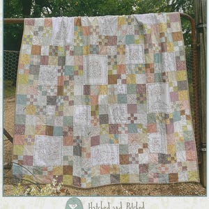 May include: A patchwork quilt with the text "SLOW & STEADY QUILT" at the top. The quilt features a variety of pastel-colored squares and embroidered panels with nature-themed designs. The quilt is displayed outdoors, draped over a metal gate.