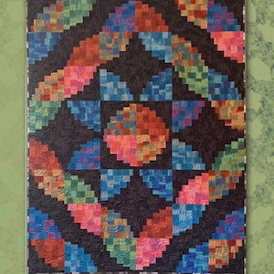 May include: A colorful quilt with a geometric design. The quilt features a central circular pattern surrounded by angled blocks in shades of blue, orange, pink, and green. The quilt measures 49.5 x 66 inches. The text "CURVY CABIN" is at the top.