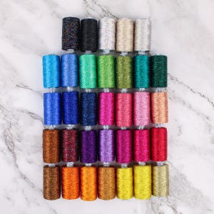May include: A collection of 36 spools of colorful thread with a glittery finish. The spools are arranged in rows of six, with each row featuring a different color scheme.