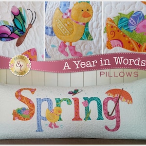 May include: A decorative pillow with the word "Spring" in colorful, patterned letters. The design includes a butterfly, duckling, and umbrella. The pillow is white with a quilted pattern and the text "A Year in Words PILLOWS".