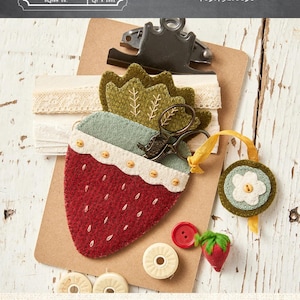 May include: A red felt strawberry scissor holder with a green leaf top, holding small scissors. The holder is on a clipboard with lace and a small flower fob. The text reads "Strawberry Scissor Holder & Fob". The holder measures 3.5" x 5.75".