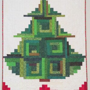 May include: A rectangular wall quilt featuring a central geometric tree design constructed from various shades of green fabric strips. The quilt has a white background and a red border. Below the quilt are two mugs and a pitcher with holly motifs.