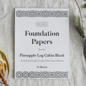 May include: A white paper pack with the text "Foundation Papers" and "Pineapple Log Cabin Block". The brand name "Jen Kingwell Designs" is at the top. The pack contains 25 sheets and is featured in Jen's Long Time Gone Pattern.