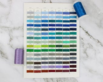 May include: A color chart with a variety of blue, green, gray, and red thread spools. The chart is labeled with the color number and name. The spools are arranged in rows and columns.