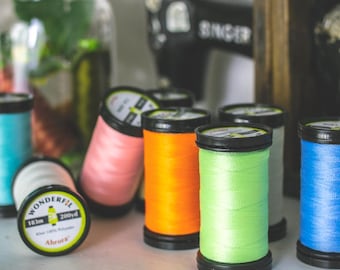 May include: Assortment of colorful spools of thread, including pink, orange, green, and blue. The spools are labeled "Wonderfil" and "Ahrora".