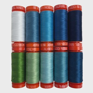 May include: A collection of Aurifil cotton thread spools in various shades of blue, green, and white. The spools are stacked in rows, with orange caps and labels. The text "Aurifil Made in Italy" and "100% Cotton" is visible on the spools.