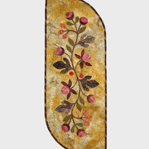 May include: A decorative table runner with a floral design. The runner features a central vine with berries and flowers in shades of pink, purple, and orange, set against a yellow background. The finished quilt size is 32" x 12". The text "Vine and Berries" is at the top.